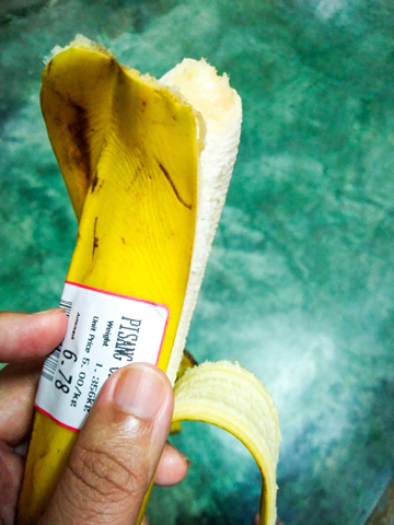 A hand is holding a partially peeled banana with a price tag indicating the weight and price.
