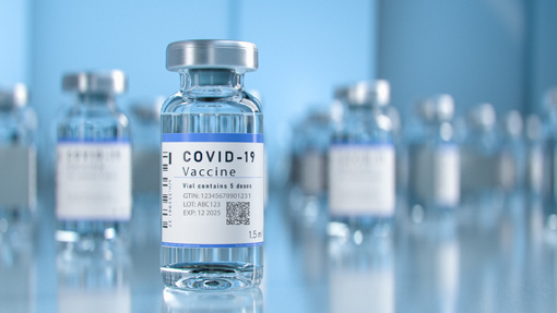 COVID-19 vaccine vials on a table, containing a clear liquid and a label with important information.