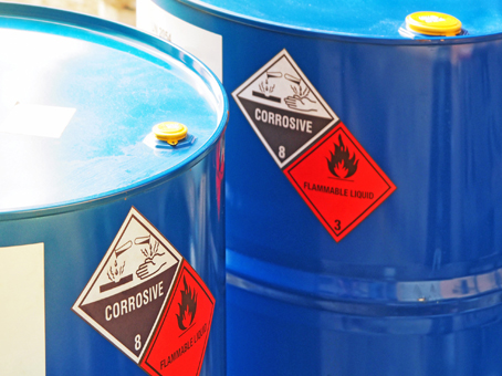 Two blue barrels with warning labels for corrosive and flammable liquids.