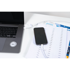 Ein Laptop und ein Smartphone liegen auf einem Tisch, verbunden durch ein Ladekabel. Neben dem Smartphone befinden sich ausgedruckte Dokumente.