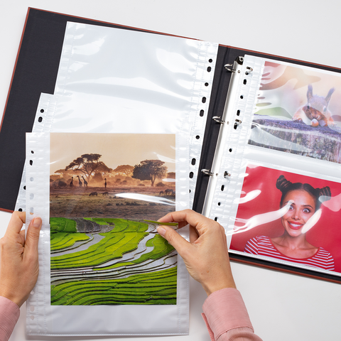 Eine Person hält ein Foto von einer Landschaft mit Reisfeldern und Bäumen, während ein Fotoalbum mit weiteren Bildern geöffnet ist.