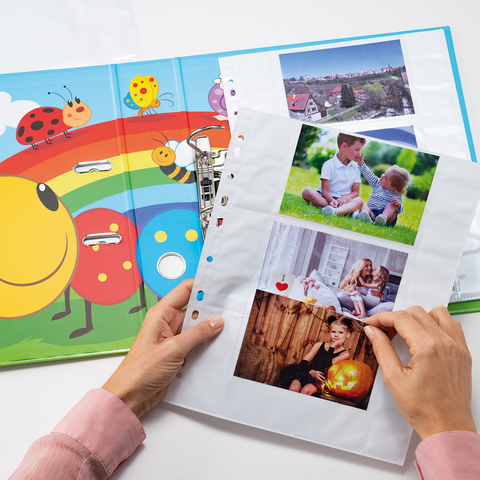 Ein offenes Bilderbuch mit bunten Illustrationen von Insekten und Blumen, daneben eine Person, die Fotos in einer transparenten Hülle betrachtet.
