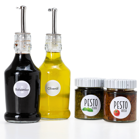 Two bottles of balsamic vinegar and olive oil, along with two jars of pesto in different varieties, set against a white background.