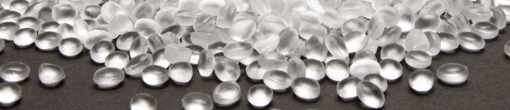 Transparent, round pearls rest on a dark surface that has a smooth and shiny texture.
