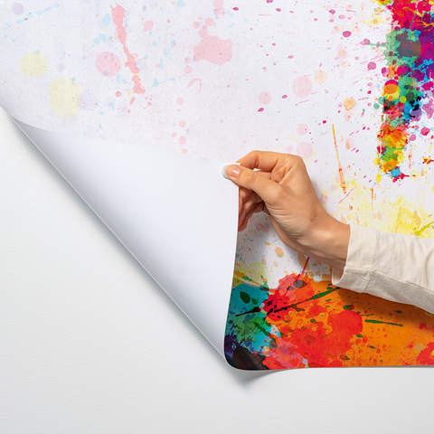 A hand pulls a large, colorful poster covered in splashes and drips from a wall.
