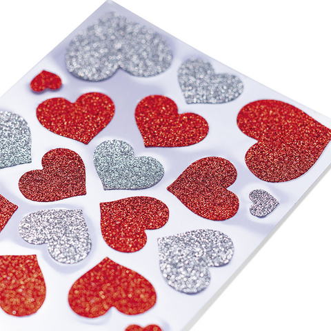 Glitzernde Herzaufkleber in verschiedenen Farben, darunter Rot, Silber und Blau, auf einem weißen Hintergrund angeordnet.
