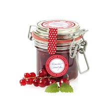 Ein Glas selbstgemachte Johannisbeermarmelade mit einem roten Etikett und frischen Johannisbeeren daneben.