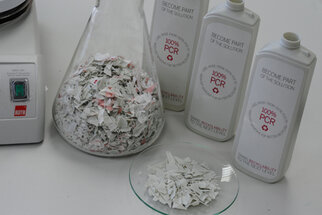A flask with crushed material and three bottles labeled '100% PCR' are sitting on a table.