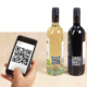 Ein Smartphone scannt QR-Codes auf zwei Weinflaschen, einer weißen und einer roten, auf einem Holztisch.