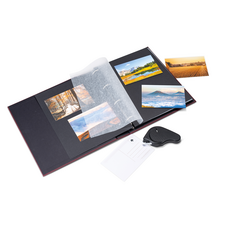 An open photo album with several pictures, a transparent protective cover, and a label. Some photos are lying next to it.