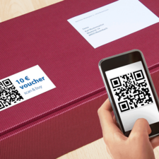 Ein rotes Paket mit einem QR-Code und einem 10 € Gutschein, während jemand mit einem Smartphone den QR-Code scannt.