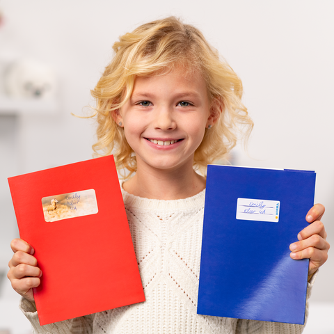 A smiling child is holding a red and a blue notebook, both covered in stickers.