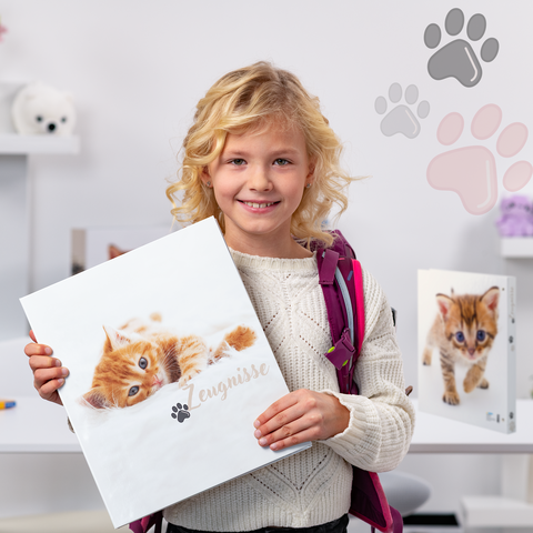 A girl with blonde curls is holding a binder featuring a picture of a cat. In the background, there are more binders and toys visible.