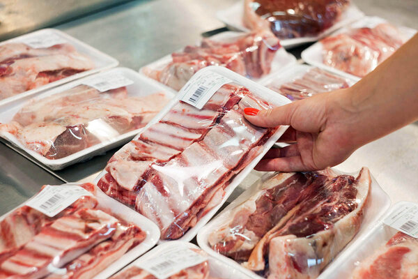 Food labeling: product label, food label on meat packaging, woman taking items from the refrigerated display.