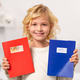 A smiling child is holding a red notebook and a blue notebook, both covered in stickers.
