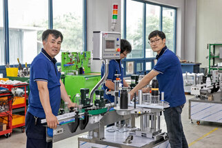 Three workers in blue shirts are operating a machinery setup in a factory, surrounded by tools and equipment.
