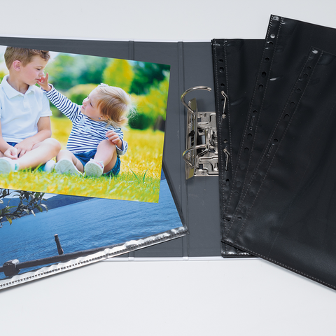 Ein Fotoalbum mit zwei Bildern: eines von zwei Kindern im Freien und eines von einer Landschaft. Leere schwarze Hüllen sind ebenfalls sichtbar.