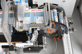 An industrial labeling machine with various rollers and a conveyor belt, used for labeling products.