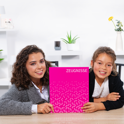 Two girls are sitting at a table holding a pink notebook with the title 'TESTIMONIALS.' They are smiling at the camera.