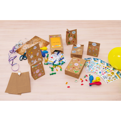 Bastelmaterialien auf einem Tisch, darunter dekorierte Papiertüten, Aufkleber, Luftballons, Scheren und bunte Süßigkeiten.