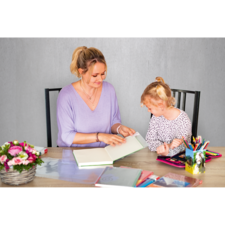 Eine Frau und ein Mädchen sitzen an einem Tisch und blättern in einem Buch. Auf dem Tisch liegen verschiedene Schreibwaren und Blumen.