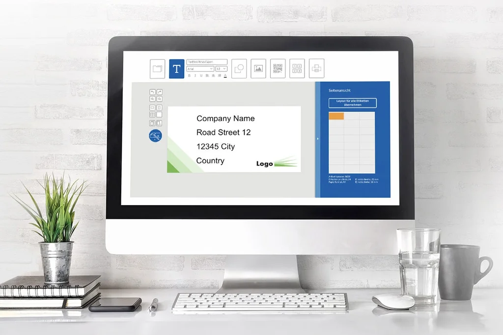 A computer screen displays a presentation with text and graphics. On the table, there are plants, notepads, and a glass of water.