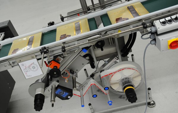 A conveyor belt with packaged products, equipped with a labeling machine and various control elements.