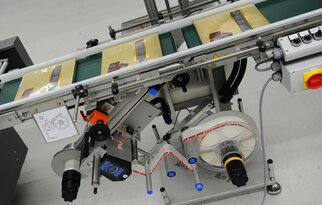 A conveyor belt with packaged products, equipped with a labeling machine and various control elements.