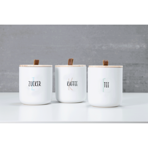 Drei weiße Behälter mit Holzdeckeln, beschriftet mit "Zucker", "Kaffee" und "Tee". Sie stehen auf einer weißen Oberfläche.