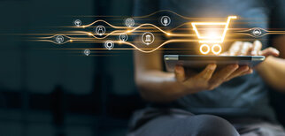 A person is holding a tablet while digital icons for online shopping and services hover around a shopping cart.