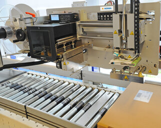 A labeling machine with a roller conveyor that applies labels to packages. The machine features digital controls and safety warnings.