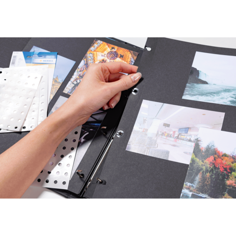 Eine Hand blättert durch einen Fotoalbum mit mehreren Bildern und Aufklebern auf schwarzem Hintergrund.