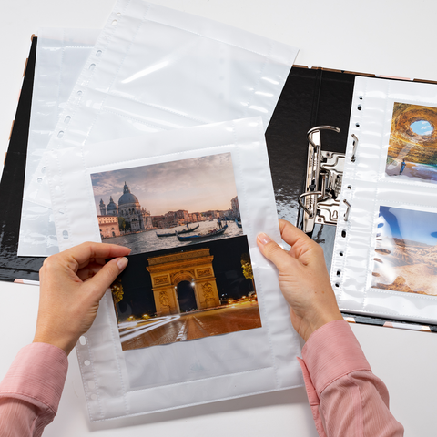 Eine Person hält Fotos in Klarsichthüllen und blättert durch ein Fotoalbum mit verschiedenen Landschaftsaufnahmen.