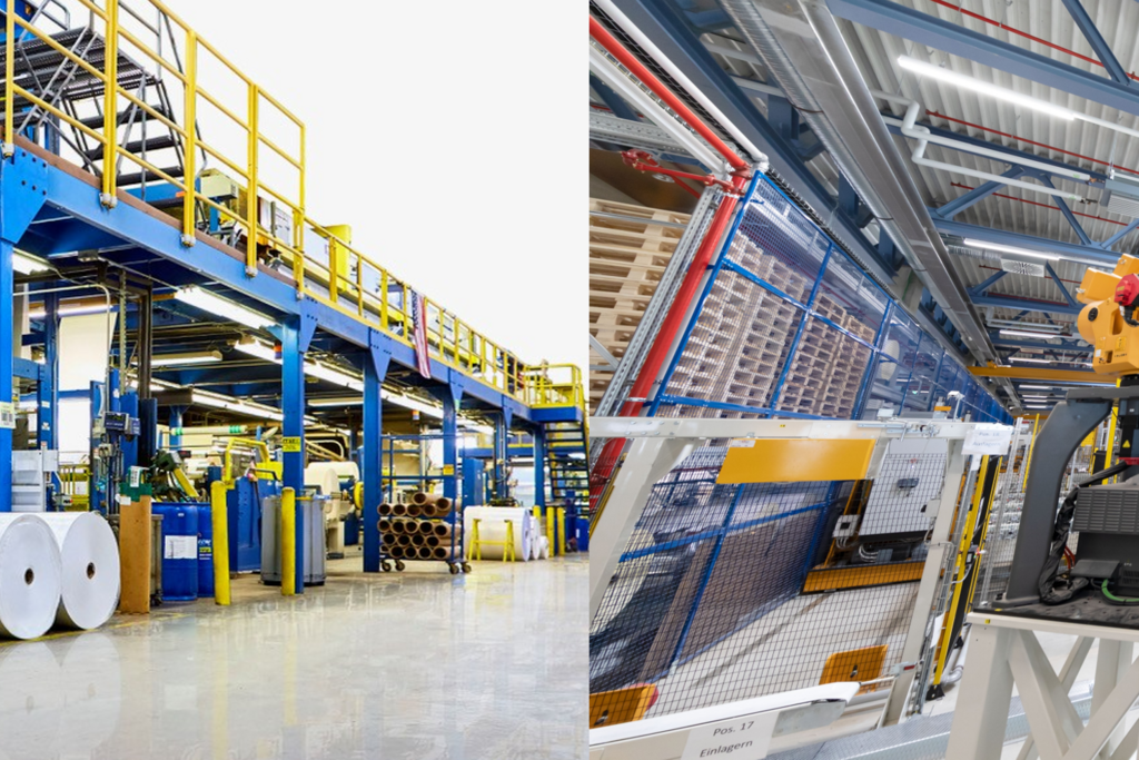 Factory hall with blue machines, large rolls of paper, and a robotic arm picking up a roll.
