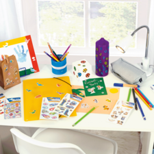 Colorfully decorated desk with craft materials, stickers, pens, a binder, and a lamp.