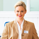 A smiling woman with blonde hair is wearing a beige blazer and a white blouse. A name tag reading 'Manuela Richter' is visible.