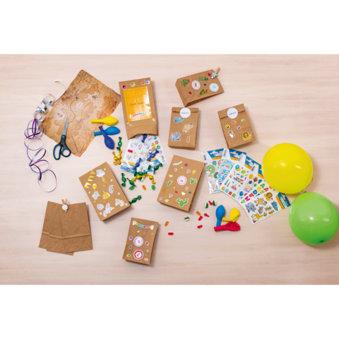 Bastelmaterialien auf einem Tisch, einschließlich Papiertüten, Aufkleber, Scheren, Bänder, Luftballons und bunte Dekorationen.