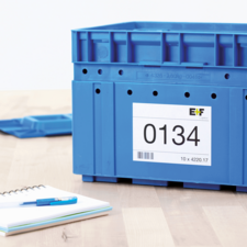 Blaue Kunststoffbox mit einer Etikette, die die Nummer 0134 zeigt, auf einem Tisch neben einem Notizblock und einem Stift.