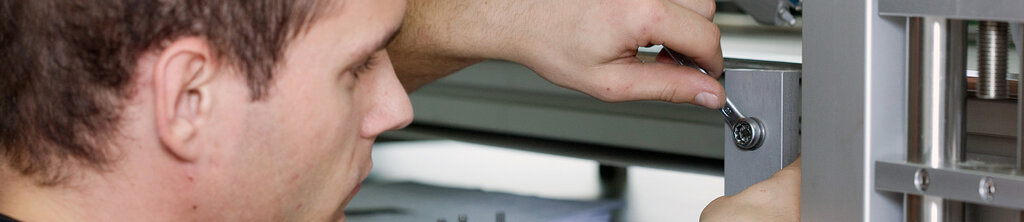 A man tightens a screw on a metal frame with a wrench.