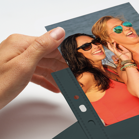A hand holds a photo of two women smiling and wearing sunglasses against a blurred background.