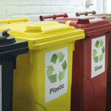 Recyclingbehälter in verschiedenen Farben für Plastik, Glas und andere Materialien, beschriftet mit entsprechenden Symbolen.