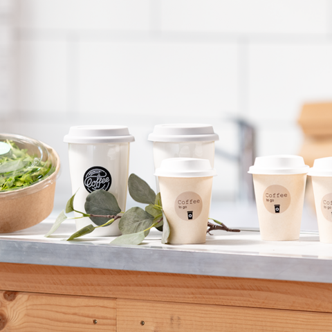 Several coffee cups are on a table next to a bowl of salad. The cups are labeled for takeout.