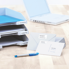 Folder with labeled compartments for incoming and outgoing documents, next to it are envelopes and a blue pen on a table.