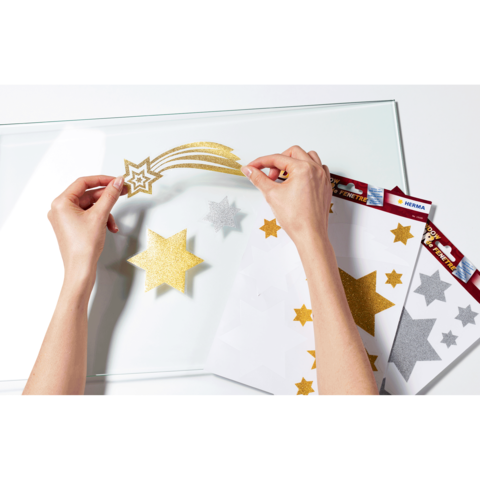 Hände platzieren goldene und silberne Sternaufkleber auf einer transparenten Oberfläche, um ein kreatives Projekt zu gestalten.