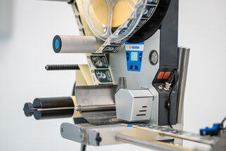 Labeling machine with rollers, control elements, and a display, ready for labeling products.
