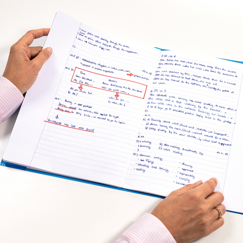 A person is holding an open notebook filled with handwritten notes and markings. The pages feature various texts and drawings.