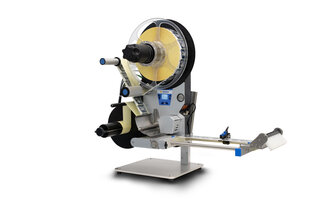 A labeling machine with rollers that applies labels to products. It features a control unit and a dispensing mechanism.