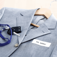 Grau Anzug mit einem Namensschild "Mr. Miller", einem Schlüsselbund und einem Schlüsselanhänger auf einem Kleiderbügel.