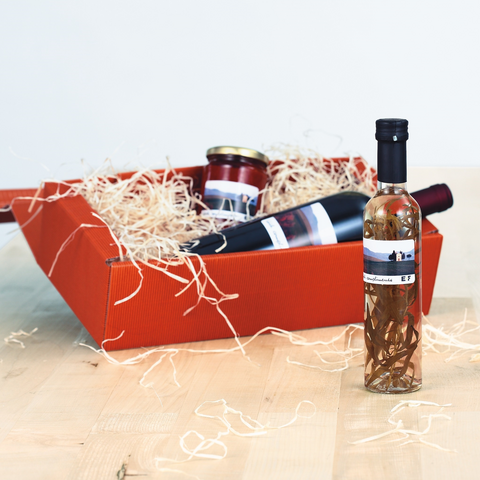 A red gift basket with a bottle, a glass, and another bottle, surrounded by wood wool. Labels are visible.