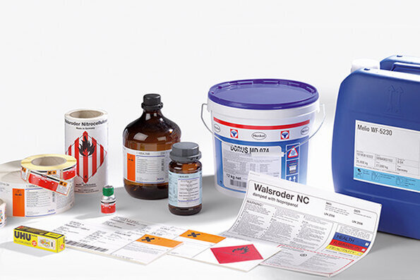 Various chemicals and containers, including bottles, buckets, and labels, arranged on a neutral surface.